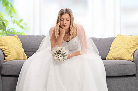 A disappointed bride sitting on a sofa looking sad, illustrating the need for a professional wedding photo retouching service UK to rescue bad photos.